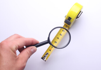 Hand with a magnifying glass examines construction tape measure