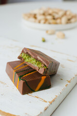 Dubai chocolate with pistachio paste and kunefe filled milk on the white cutting board on the table. Popular food concept. Vertical orientation. Selective focus.