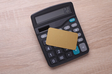 Obraz premium Black classic calculator with golden business card on table. Top view