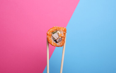 Chinese chopsticks holding sushi roll on pink blue background