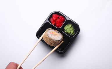 Hand holding sushi roll with chopsticks, Tray with ginger, wasabi and soy sauce on white background