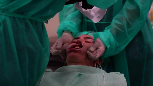 Rack focus shot of dentist photographing patient's mouth while assistant uses cheek retractor