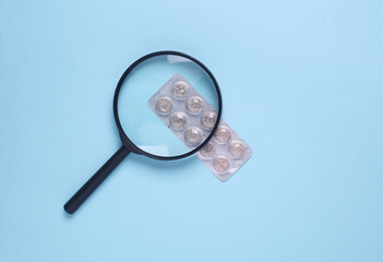 Magnifying glass with blister of pills on blue background