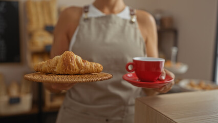 Woman holding croissant and red coffee cup in a bakery interior