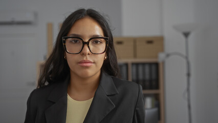 Young woman with glasses in an office environment, showcasing a professional and focused demeanor,...