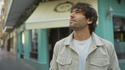Young man stands outdoors on city street looking hopeful surrounded by urban architecture and...