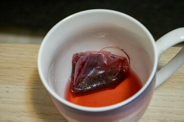 A close-up of a tea bag steeping in a cup, creating a rich red color. Perfect for representing relaxation and comfort with beverages.