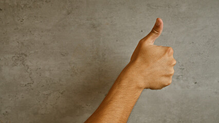Thumb showing positive gesture against textured concrete background, conveying approval and...