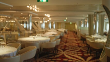 Blurred view of a luxurious restaurant interior featuring elegant tables with decorated settings, highlighting the sophisticated ambiance and stylish decor elements.