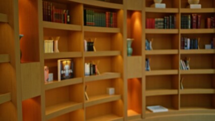 Blurry view of a library's wooden bookshelves filled with various books creates a serene indoor atmosphere with a defocused ambiance.