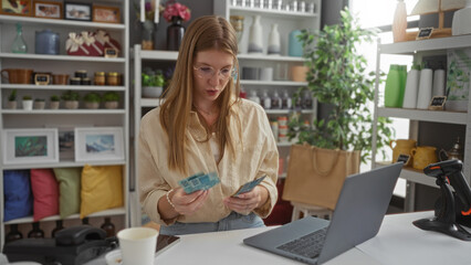 Young, blonde, woman examining currency in a home decor store with shelves filled with colorful pillows and various decorative items