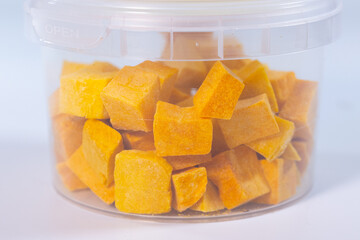 A clear container filled with freeze-dried pumpkin cubes, offering a convenient and nutritious snack or cooking ingredient. Bright orange color highlights freshness.