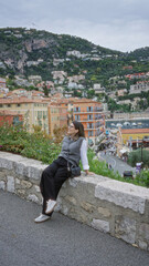 Obraz premium Woman smiling in villefranche france with scenic european seaside view showcasing colorful architecture and vibrant hillside.