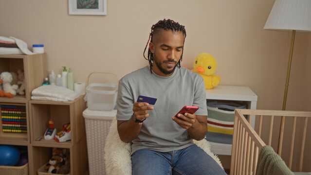 Young man using phone near cradle in bedroom with baby toys around for online purchase with credit card showing modern lifestyle indoors at home. - Powered by Adobe