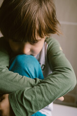 Little boy toddler is sitting alone on the floor and hugging his knees after suffering an act of bullying.