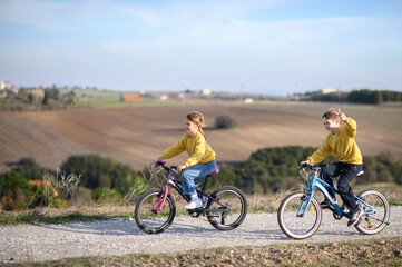 Obraz premium A boy and a girl race their bicycles through the countryside at sunset, laughing and chasing each other. The golden light and peaceful surroundings create a joyful, carefree moment of childhood advent