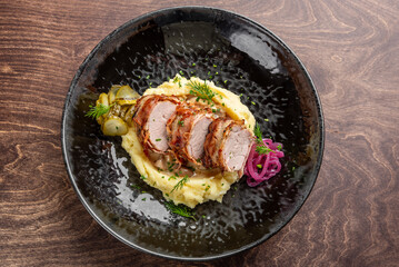 A gourmet dish featuring sliced roasted meat on a bed of creamy mashed potatoes, garnished with...