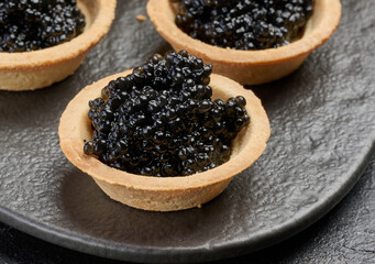 Black sturgeon caviar in round tartlets on table, top view