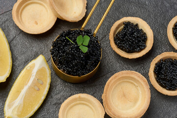 Black sturgeon caviar and empty round tartlets on table, top view