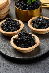 Black sturgeon caviar in round tartlets on table, top view