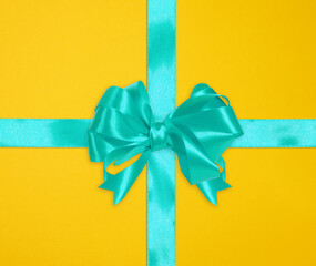 Tied bow made of blue silk ribbon on yellow background, decor for a gift