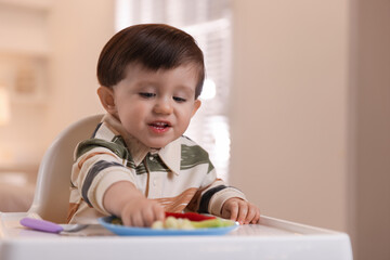 Naklejka premium Cute little baby eating healthy food in high chair at home