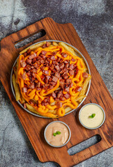 Porção de batata frita com queijo cheddar e bacon servida com molho de maionese e molho rose
