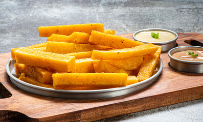 Porção de polenta frita  servida molho de maionese, sobre tábua de madeira
