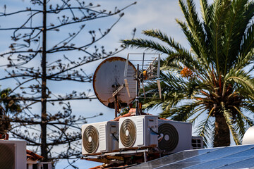A satellite dish is mounted on a rooftop with two air conditioners