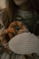 A young girl holds a fresh cinnamon pretzel in her hands, decorated with a Christmas tree branch.