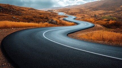 Scenic winding road through autumn landscape with golden grasses and distant hills under a cloudy sky