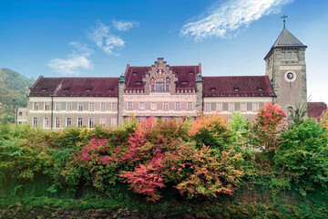 Historic clock tower building in Feldkirch, Austria surrounded by vibrant autumn foliage, picturesque mountain backdrop, and classic European architecture showcasing timeless beauty