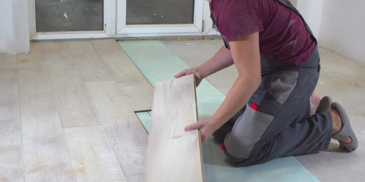 Construction worker installing laminate flooring over green underlay