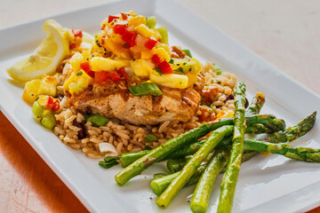 grilled salmon topped with pineapple salsa on a bed of seasoned rice with a side of asparagus
