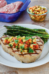 grilled swordfish topped with mango salsa served with asparagus on a white plate