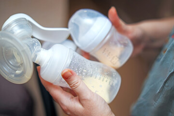 woman's hands hold a manual breast pump and a bottle containing drops of breast milk, symbolizing breastfeeding and nurturing for infants