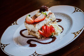 tiramisu topped with fresh strawberries and chocolate sauce