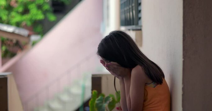 Young child covering her face with hands, sitting on the floor in emotional distress, reflecting in a peaceful but somber outdoor urban setting, experiencing sadness and trauma
