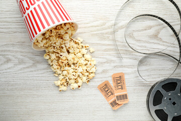 Tasty popcorn, tickets and film reel on white wooden background, flat lay