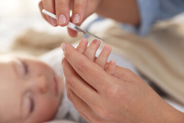Mother cutting her cute little baby's nails on bed, closeup