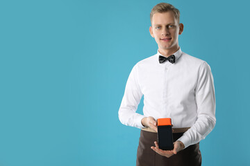 Happy waiter with payment terminal on light blue background, space for text