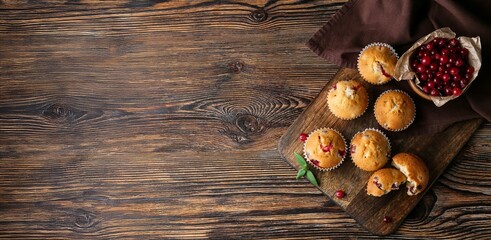 Tasty cranberry muffins on wooden background with space for text, top view