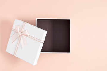 Open white square gift box with a satin ribbon on an isolated pastel pink background. Mother's day,...