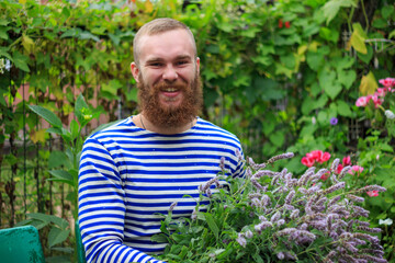 A man with a red beard laughs, holds a large bouquet of flowers, close-up portrait of a man, joy, happiness, summer, nature.