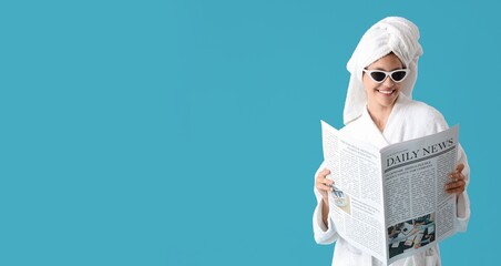 Pretty young woman in bathrobe reading newspaper on blue background with space for text