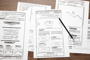 Developing UI design. Sketches of website wireframes and pencil on wooden table, top view