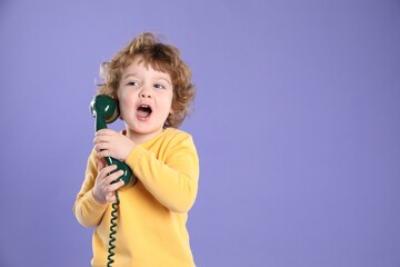Cute little boy with telephone handset on violet background, space for text
