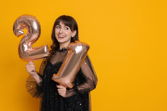 Coming of age party - 21st birthday. Young woman holding number shaped balloons on yellow background, space for text