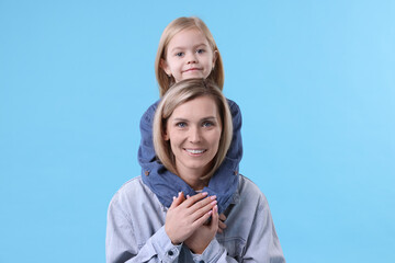 Cute little girl hugging her mom on light blue background. Happy Mother's Day