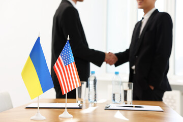 Diplomats shaking hands during meeting indoors, focus on flags of USA and Ukraine